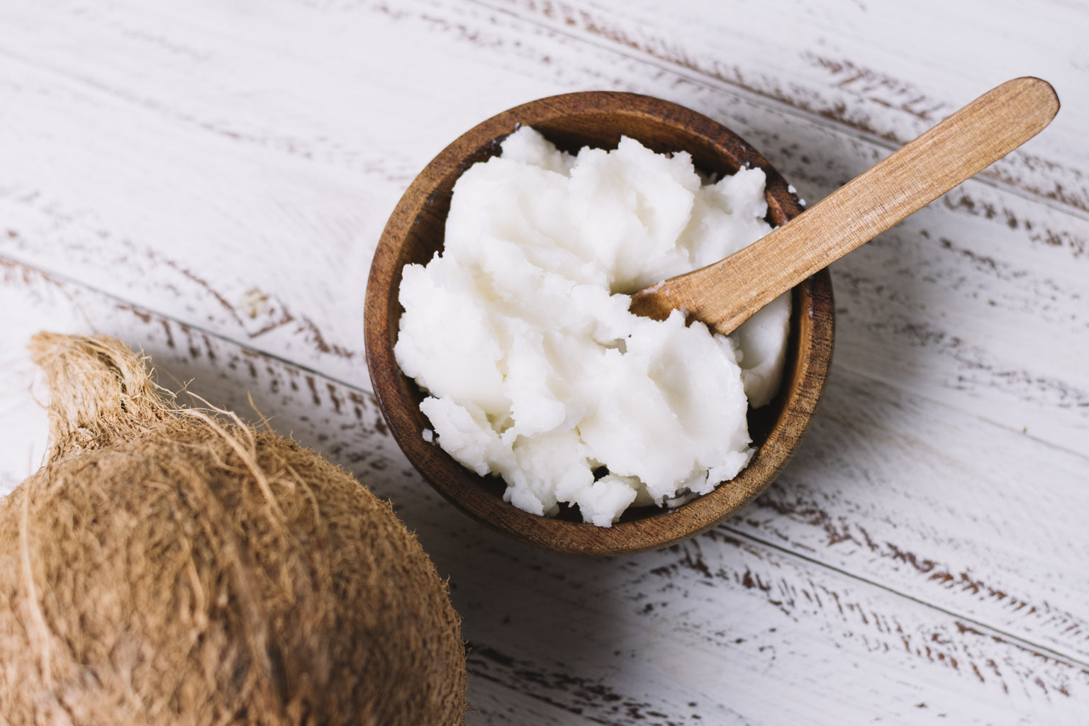 Coconut oil in a wooden bowl with a wooden spoon on a rustic wooden surface