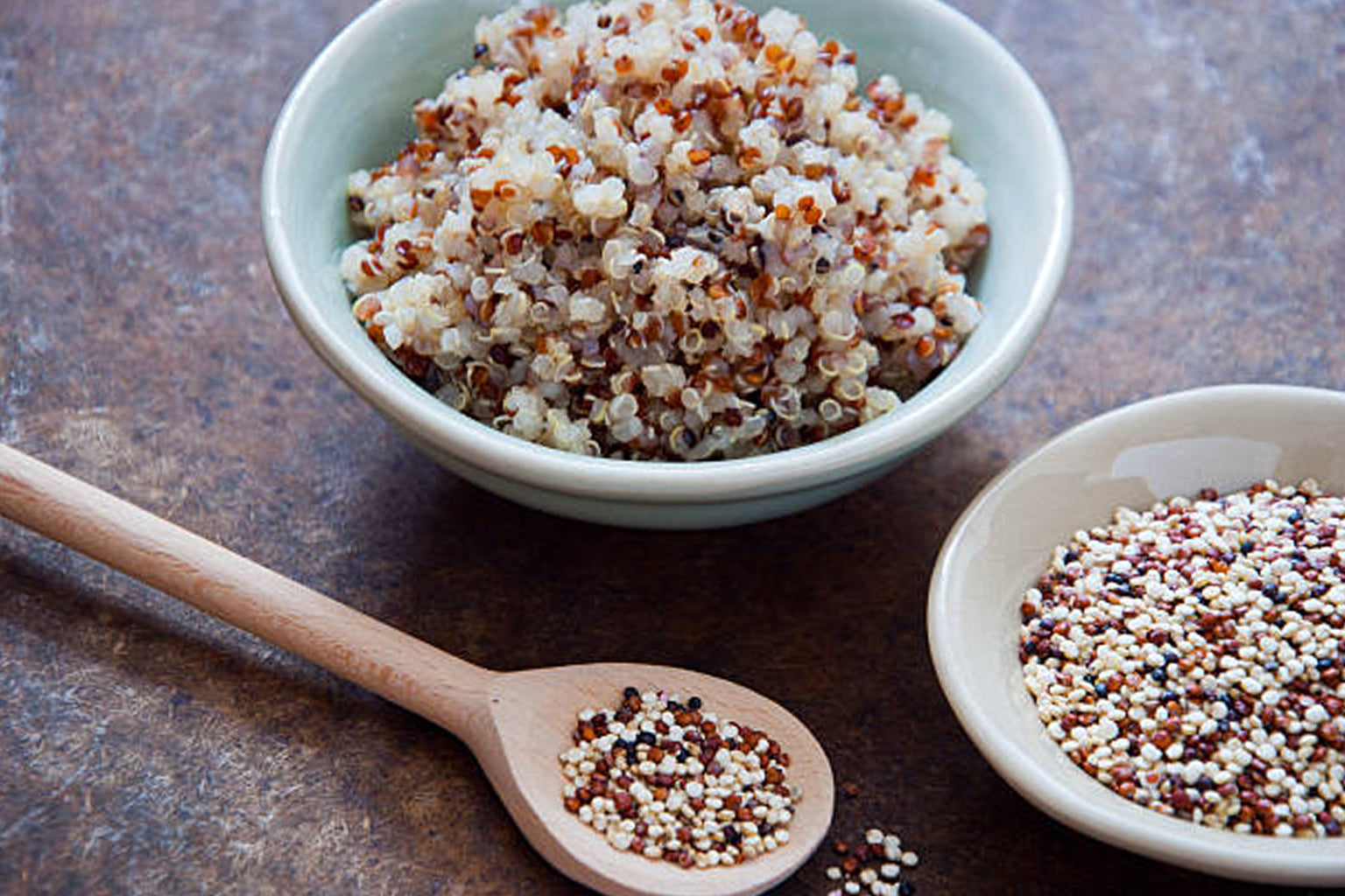 Bowl of multicolored quinoa with a wooden spoon on a textured surface