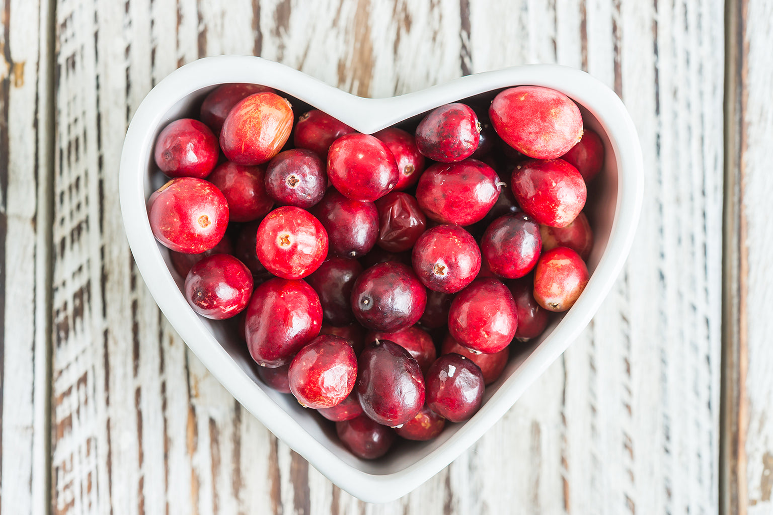 Heart-shaped bowl filled with red cranberries on a wooden surface