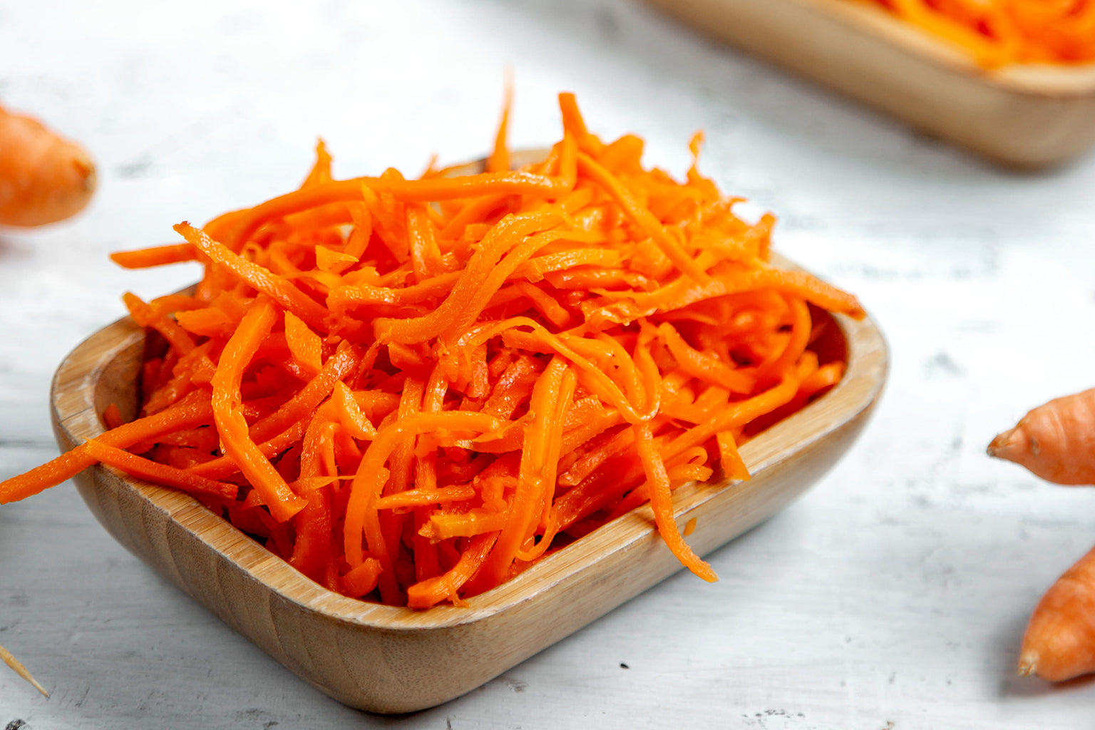 Shredded carrots in a wooden bowl on a light background