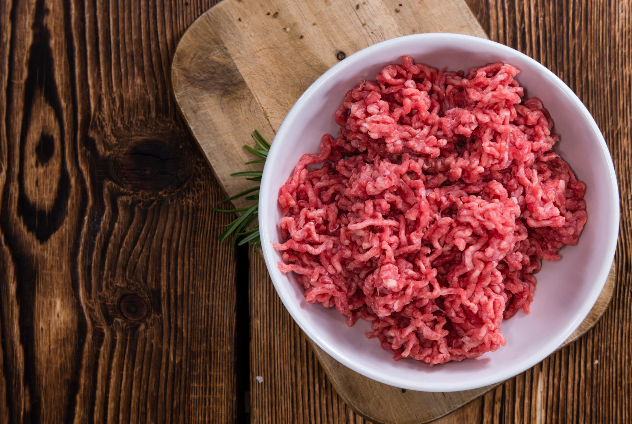 Ground beef in a white bowl on a wooden cutting board