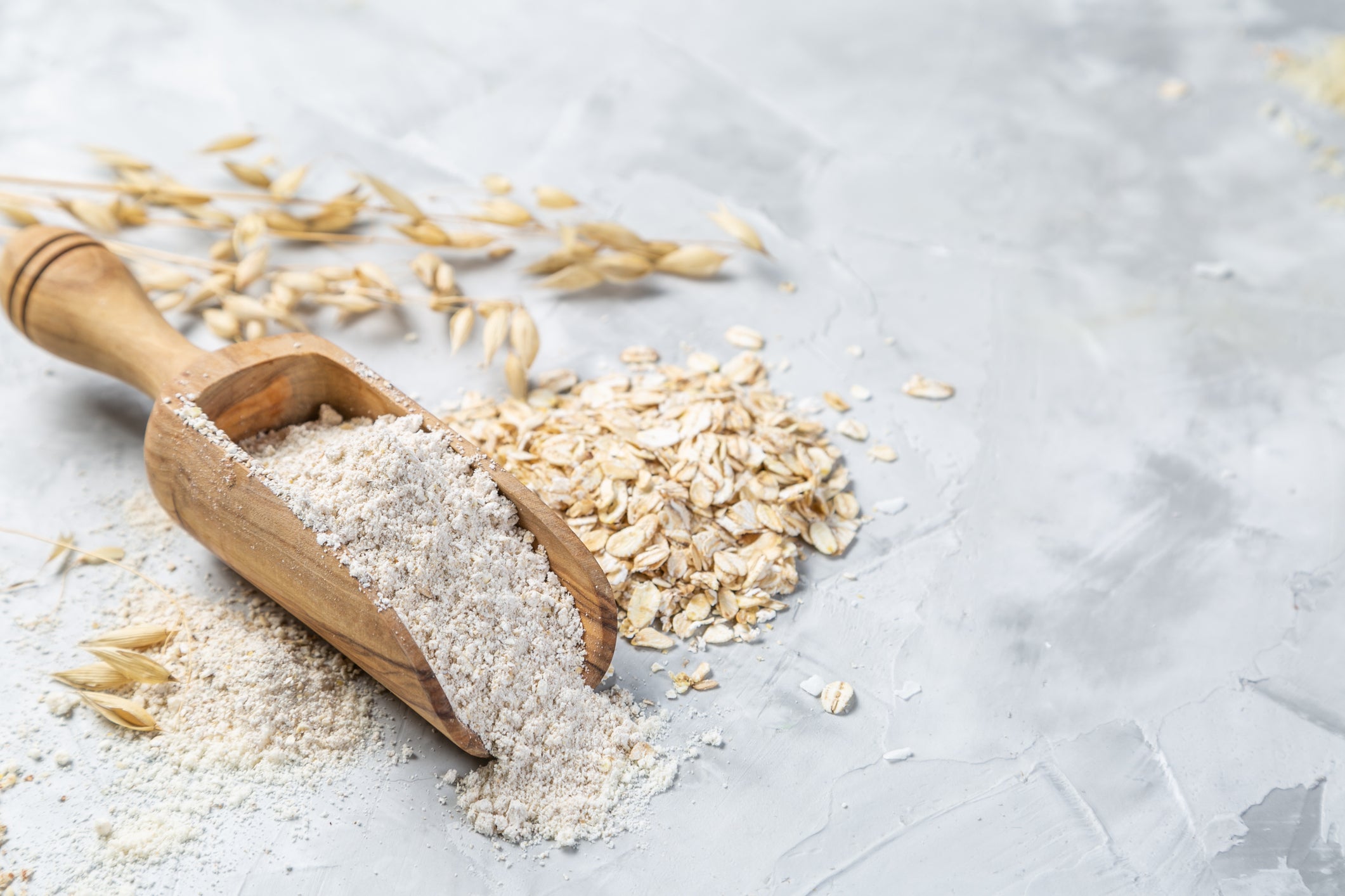 Wooden scoop with rolled oats on a light gray surface