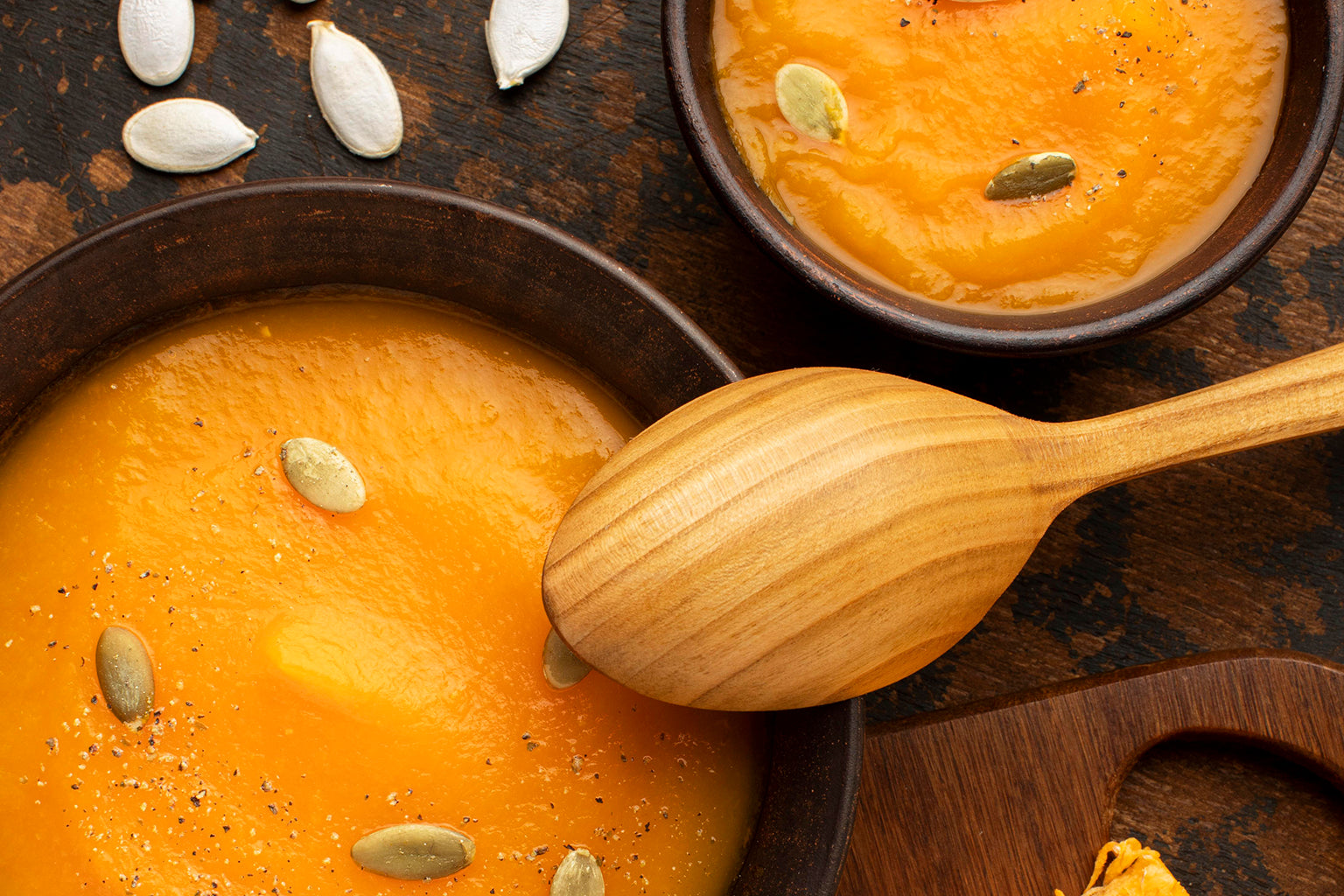 pumpkin puree soup in a bowl with wooden spoon and pumpkin seeds on a rustic background