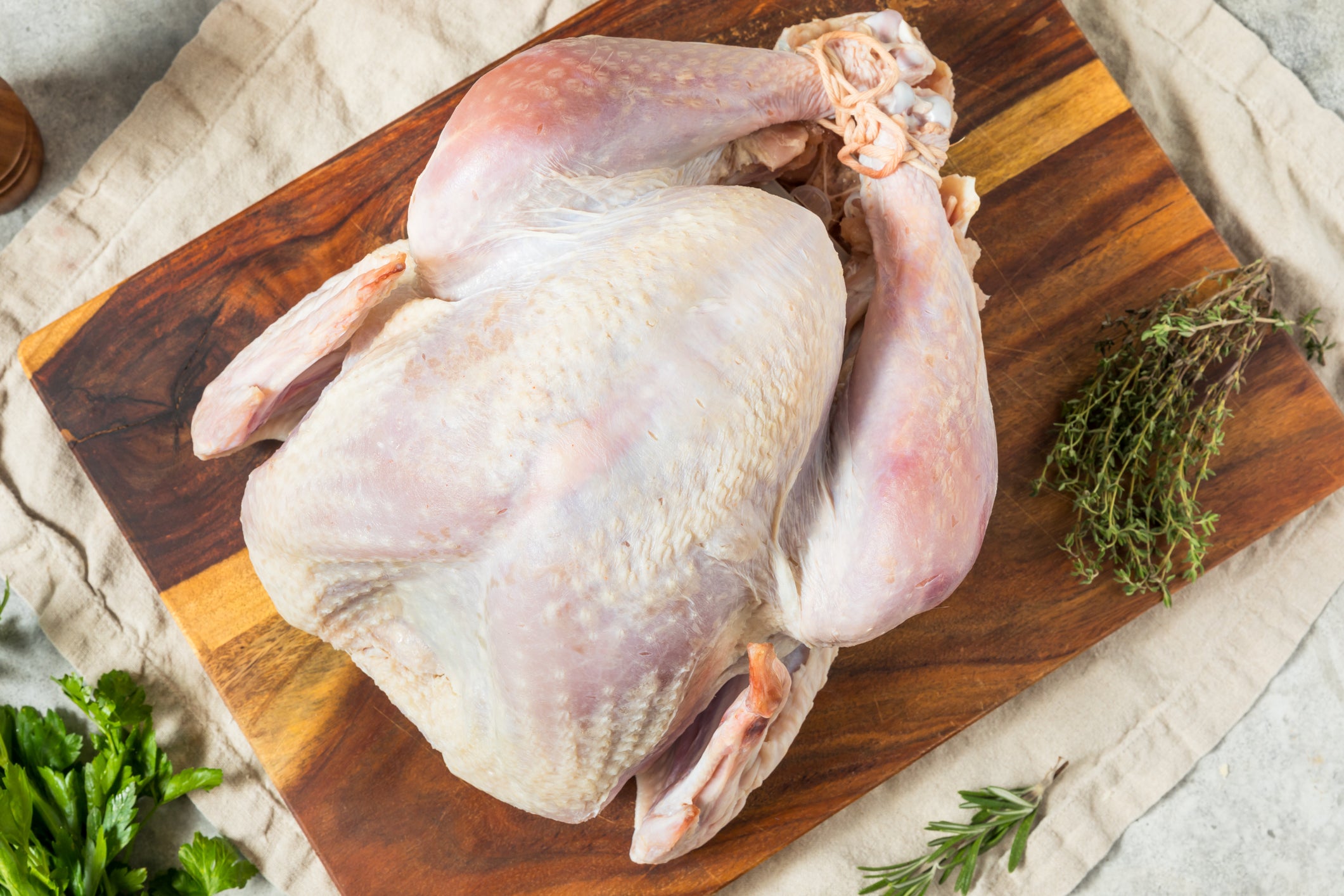 Raw turkey on a wooden cutting board with herbs