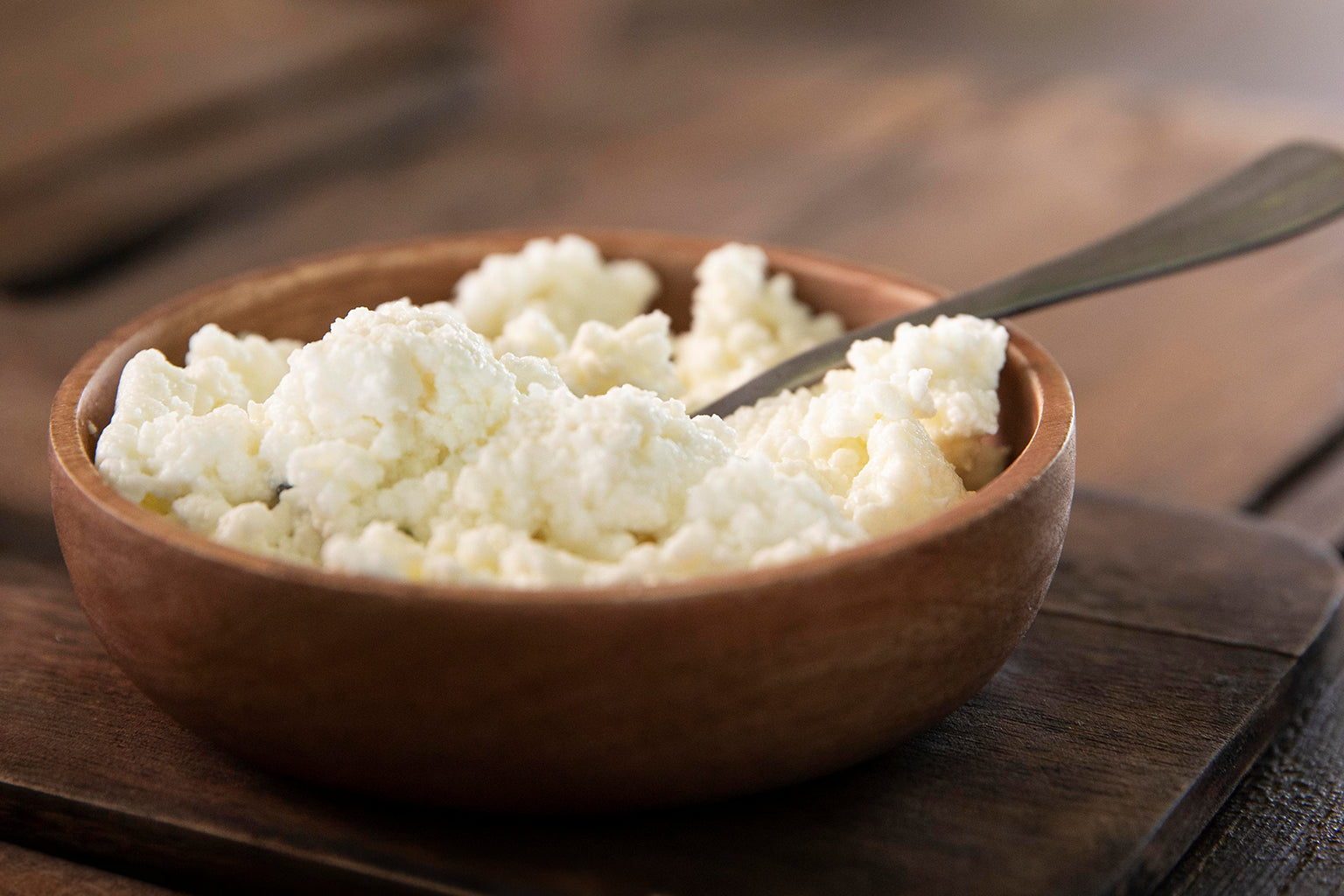 wooden bowl of cottage cheese with spoon on wood platter