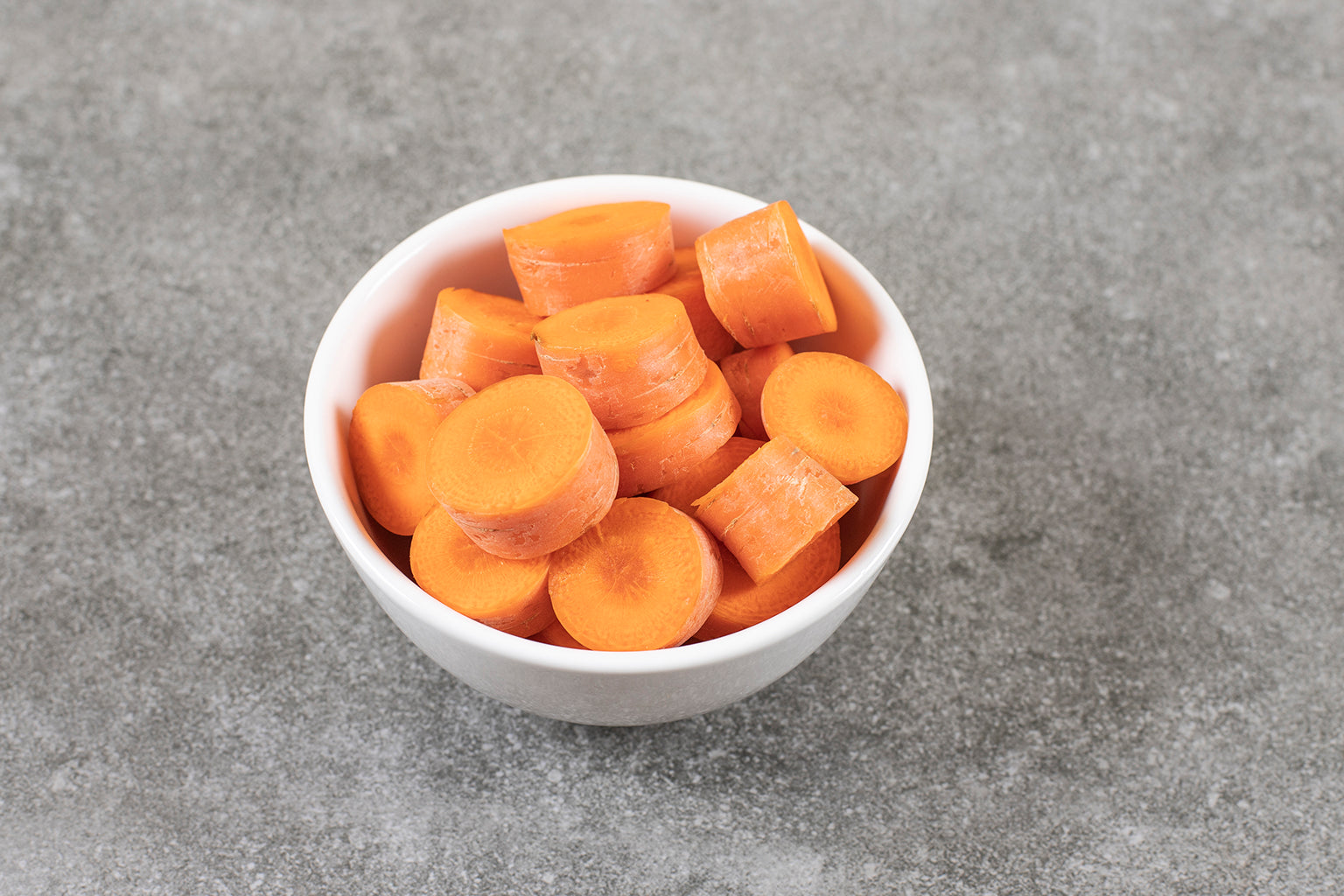 White bowl filled with chopped carrots on a gray surface