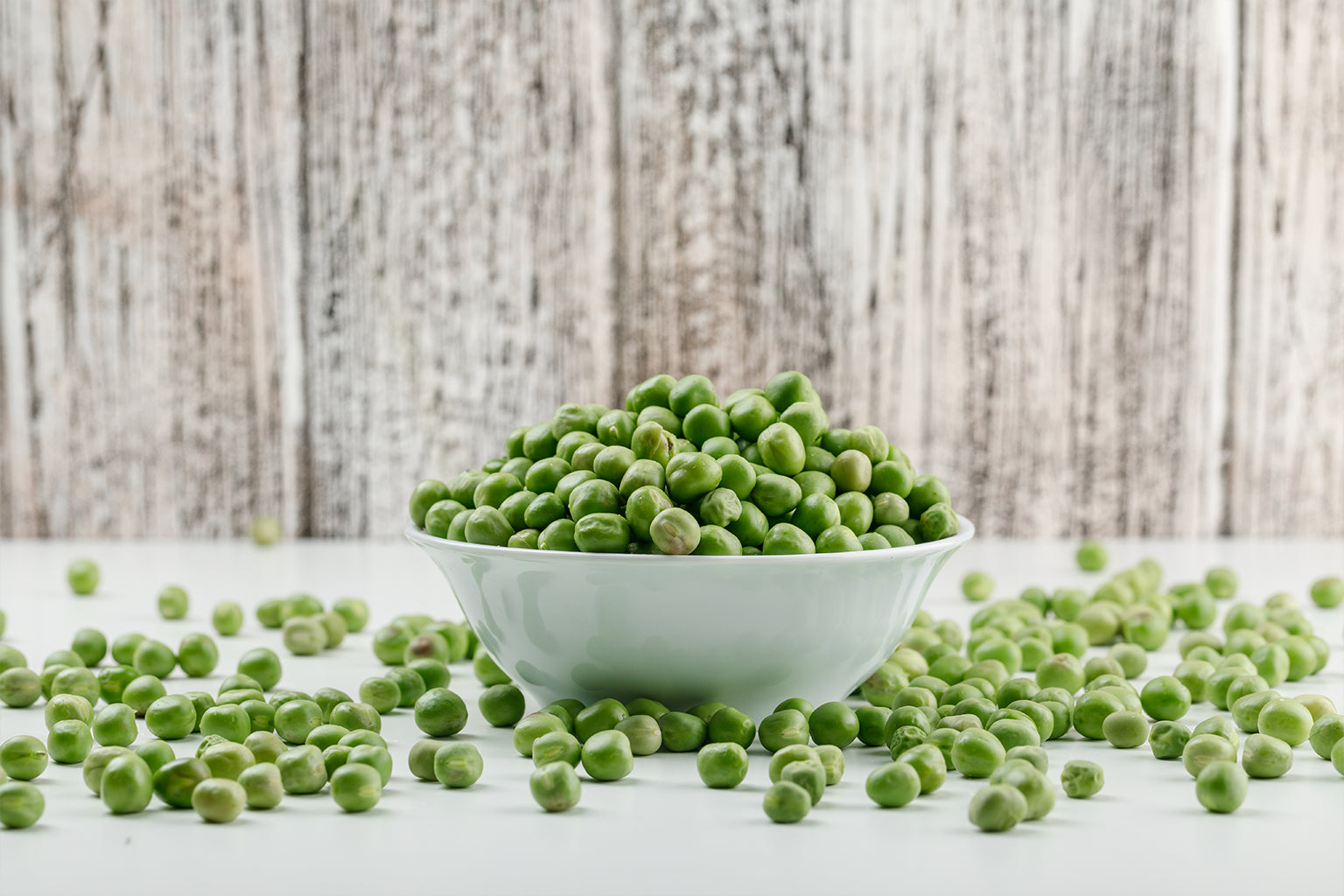 Bowl of green peas on a wooden surface