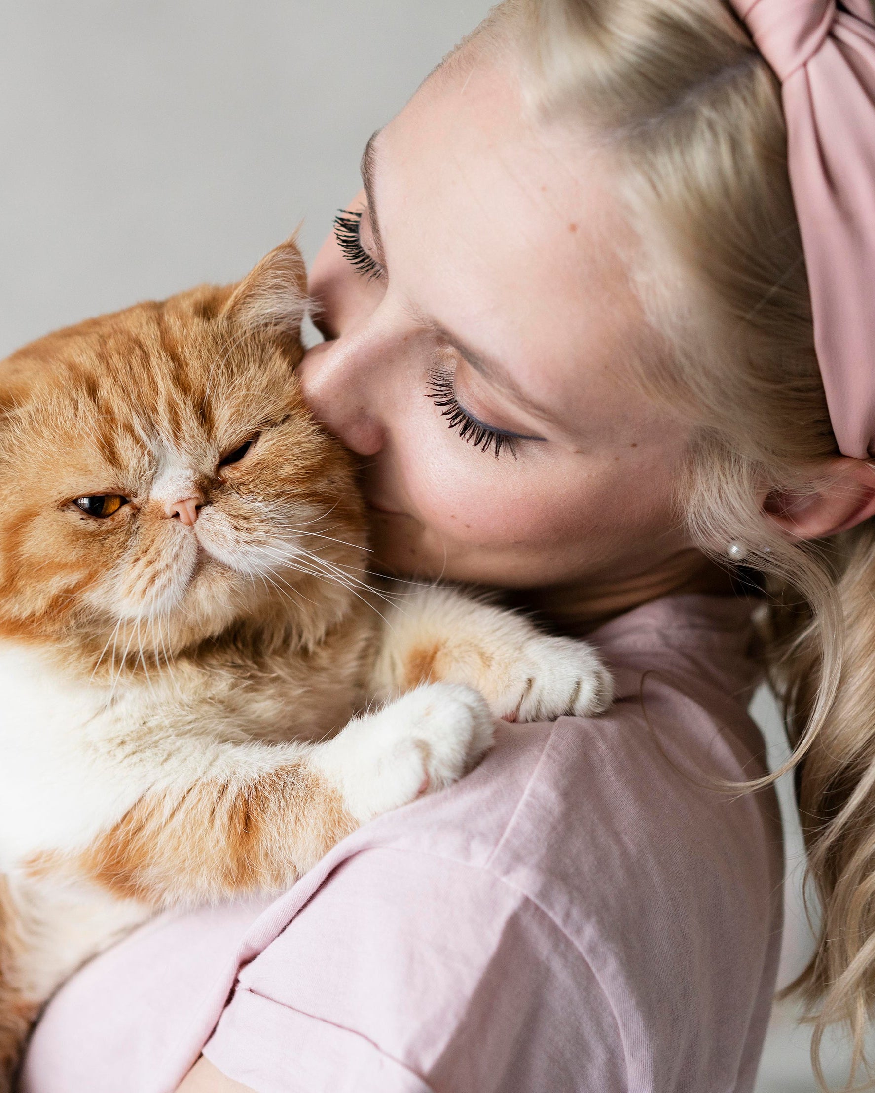 Woman kissing an orange cat on a light gray background