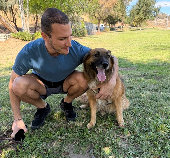 Man in a blue shirt kneeling on grass with a brown dog.